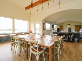 A dining area with a large wooden table surrounded by chairs next to large windows and a living space with sofas and lamps at WildLuing in Cullipool Isle Of Luing