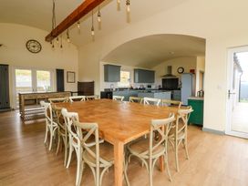 A kitchen and dining area with a large wooden table and chairs under hanging light bulbs at WildLuing in Cullipool Isle Of Luing