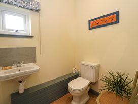 A bathroom with a toilet a small sink a window a chair with a plant and a framed picture at WildLuing in Cullipool Isle Of Luing