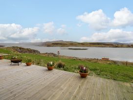 A wooden deck with flower pots overlooking a grassy area and a body of water with hills in the background at WildLuing in Cullipool Isle Of Luing