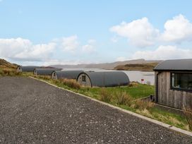 A row of curved cabins on grass near water with gravel path at WildLuing Cullipool Isle Of Luing
