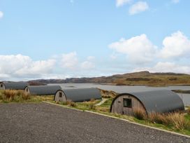 A row of curved wooden cabins near water with hills in the background at WildLuing in Cullipool Isle Of Luing