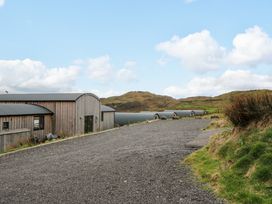 A gravel road leading past wooden buildings with curved roofs and hills in the background at WildLuing in Cullipool Isle Of Luing
