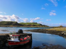 A fishing boat docked by a stone pier in a coastal inlet with grassy hills in the background at WildLuing Cullipool Isle Of Luing