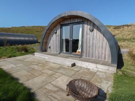A curved wooden cabin with glass doors on a stone patio with a fire pit in front in a grassy area at WildLuing Cullipool Isle Of Luing