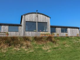 A wooden building with large windows and flower pots on a deck overlooking grass at WildLuing Cullipool Isle Of Luing