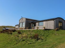 A wooden cabin with large windows and flower pots on a deck in a grassy area at WildLuing in Cullipool Isle Of Luing