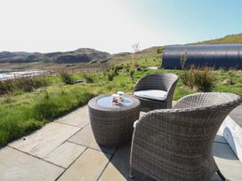 An outdoor patio with wicker chairs and a table with two cups overlooking grassy hills and a large curved structure at WildLuing Cullipool Isle Of Luing