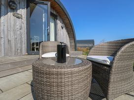 Two wicker chairs with cushions and a wicker table with a black coffee maker on a patio outside a wooden pod at WildLuing Cullipool Isle Of Luing