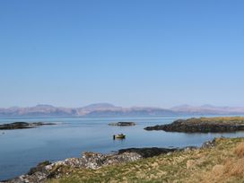 A small boat floating on a calm body of water near rocky shorelines with mountains in the background at WildLuing in Cullipool Isle Of Luing