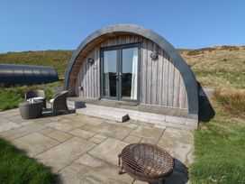 An arched wooden cabin with glass doors a small patio with two chairs a table and a fire pit at WildLuing Cullipool Isle Of Luing
