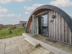 An arched wooden cabin with a glass door open onto a stone patio and grassy landscape at WildLuing Cullipool Isle Of Luing