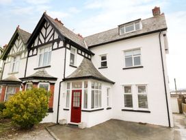 A semi detached house with white walls black trim and a red front door at 51 Trinity Avenue in Llandudno