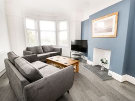 A living room with gray sofas a wooden coffee table a TV on a stand and a blue accent wall at 51 Trinity Avenue in Llandudno