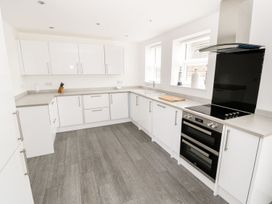 A kitchen with white cabinets a stove and a wooden cutting board at 51 Trinity Avenue in Llandudno