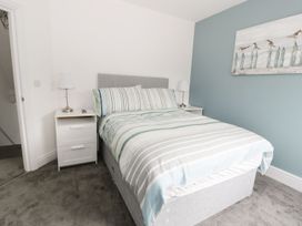 A bedroom with a bed with striped bedding two bedside tables with lamps and a blue accent wall with bird artwork at 51 Trinity Avenue in Llandudno
