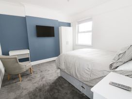 A bedroom with a bed a chair a desk a wardrobe a wall-mounted TV and a window at 51 Trinity Avenue in Llandudno
