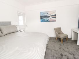 A bedroom with a bed striped bedding a grey chair a landscape picture on the wall and a white desk at 51 Trinity Avenue in Llandudno