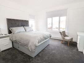 A bedroom with a large bed with grey headboard grey bedding a grey carpet two white nightstands with lamps a grey chair and a white desk at 51 Trinity Avenue in Llandudno