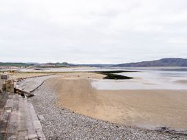 A beach with sand and pebbles next to a sea wall with steps and a person sitting at 51 Trinity Avenue in Llandudno