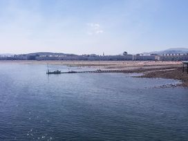 A coastline with a long row of buildings along the shore a pier extending into the water and hills in the background at 51 Trinity Avenue in Llandudno