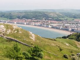A coastal town with buildings along a curved beach and hills with greenery in the foreground at 51 Trinity Avenue in Llandudno