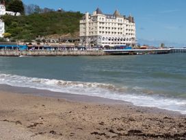 A beach with waves in front of a pier and a large hotel on a hillside at 51 Trinity Avenue in Llandudno