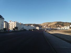 A promenade with white buildings on one side and a beach on the other with hills in the background at 51 Trinity Avenue in Llandudno