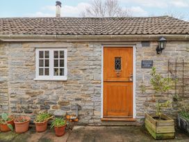 Stone cottage exterior with a wooden door a white window potted plants and a sign reading Honeysuckle Cottage at Compton Dundon near Street
