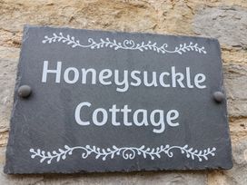 A black slate house name sign with white text and decorative border reading Honeysuckle Cottage on a stone wall at Honeysuckle Cottage in Compton Dundon near Street