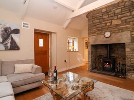 A living room with a stone fireplace a wooden door a gray sofa a glass coffee table with a wine bottle and glasses and a painting of a cow at Honeysuckle Cottage Compton Dundon near Street