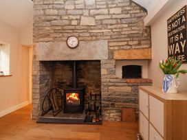 A stone fireplace with a wood-burning stove fire and log holder next to a cabinet with a vase of tulips and wall art at Honeysuckle Cottage in Compton Dundon near Street