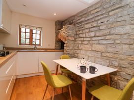 A kitchen with a white table and green chairs next to a stone wall at Honeysuckle Cottage Compton Dundon near Street