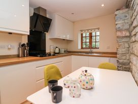 A kitchen with white cabinets wooden countertop a window and a white table with cups and a teapot at Honeysuckle Cottage in Compton Dundon near Street