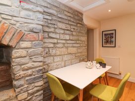 A dining area with a white table and green chairs next to a stone wall with teapots and cups on the table at Honeysuckle Cottage in Compton Dundon near Street