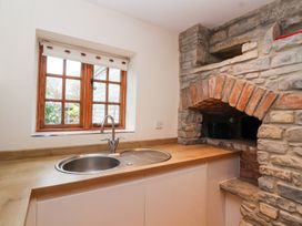 A kitchen sink with a wooden countertop and a window above next to a stone wall with an arch at Honeysuckle Cottage in Compton Dundon near Street