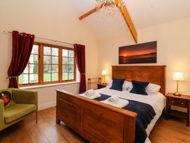 A bedroom with a wooden bed and side tables with lamps near a window with red curtains and a green armchair at Honeysuckle Cottage in Compton Dundon near Street