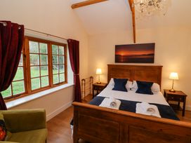 A bedroom with a wooden bed and side tables with lamps next to a window with red curtains at Honeysuckle Cottage in Compton Dundon near Street