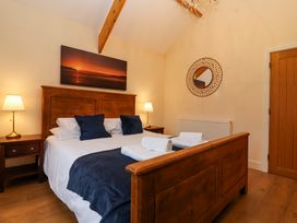 A bedroom with a wooden bed frame two bedside tables with lamps a round mirror and a sunset painting at Honeysuckle Cottage in Compton Dundon near Street