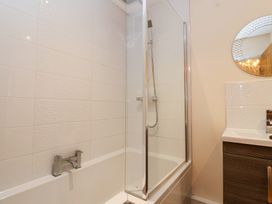 A bathroom with a bathtub and shower with glass screen and a sink with a round mirror at Honeysuckle Cottage in Compton Dundon near Street