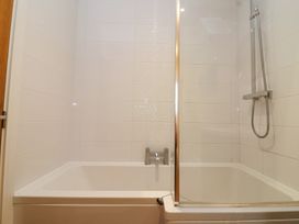 A white tiled bathroom with a bathtub and a shower at Honeysuckle Cottage in Compton Dundon near Street