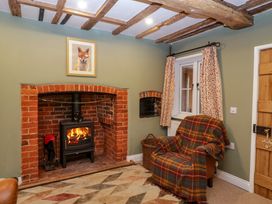 A room with a brick fireplace with a wood stove fire armchair with a plaid blanket window with curtains and wooden ceiling beams at 2 Loxter Villas in Wellington Heath near Ledbury