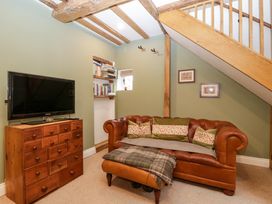 A living room with a brown leather sofa with cushions a wooden chest of drawers with a TV and bookshelves under exposed wooden beams at 2 Loxter Villas Wellington Heath near Ledbury