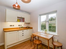 A kitchen with white cabinets a wooden countertop a wooden table with stools and a window showing a garden at 2 Loxter Villas Wellington Heath near Ledbury