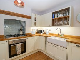 A kitchen with white cabinets wooden countertops a built in oven and stove a double sink and an open shelf with plates and jars at 2 Loxter Villas Wellington Heath near Ledbury