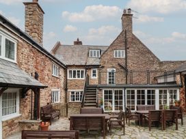 An outdoor stone courtyard with wooden tables and benches in front of a stone building at Dragon House in Bilbrook near Minehead