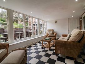 A sitting room with wicker furniture and large windows overlooking a garden at Dragon House in Bilbrook near Minehead