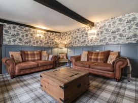 A living room with two brown leather sofas a wooden coffee table a patterned armchair and wallpaper with horse riders at Dragon House in Bilbrook near Minehead