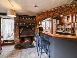 A small bar area with wooden stools and a fireplace with stacked firewood at Dragon House in Bilbrook near Minehead