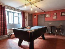 A game room with a pool table, wooden chairs, a round table, framed pictures on the wall, and windows with curtains at Dragon House in Bilbrook near Minehead